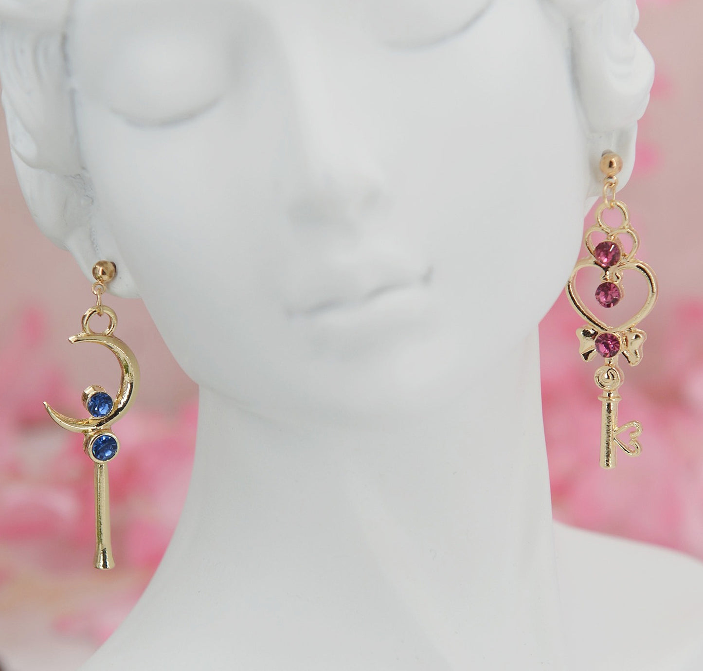 Asymmetrical earrings, inspired by the warriors' scepter from Sailor Moon. One earring features a sleek, scepter design with delicate details, the other showcases a crescent moon charm for a celestial touch.