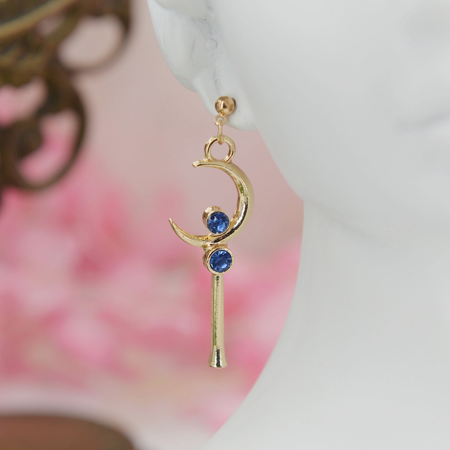 Asymmetrical earrings, inspired by the warriors' scepter from Sailor Moon. One earring features a sleek, scepter design with delicate details, the other showcases a crescent moon charm for a celestial touch.